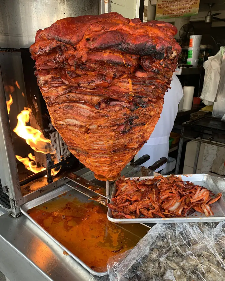Trompo de carne al pastor girando frente a la flama, con la piña arriba